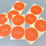 Sticker rond 50mm `Hello i`m here` oranje met lichtroze letters  ( set van 10 stuks )